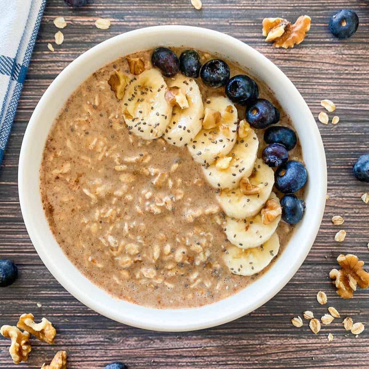 Bowl of creamy oats topped with banana slices, nut butter, seeds, and nuts served as a pre-workout energy meal.